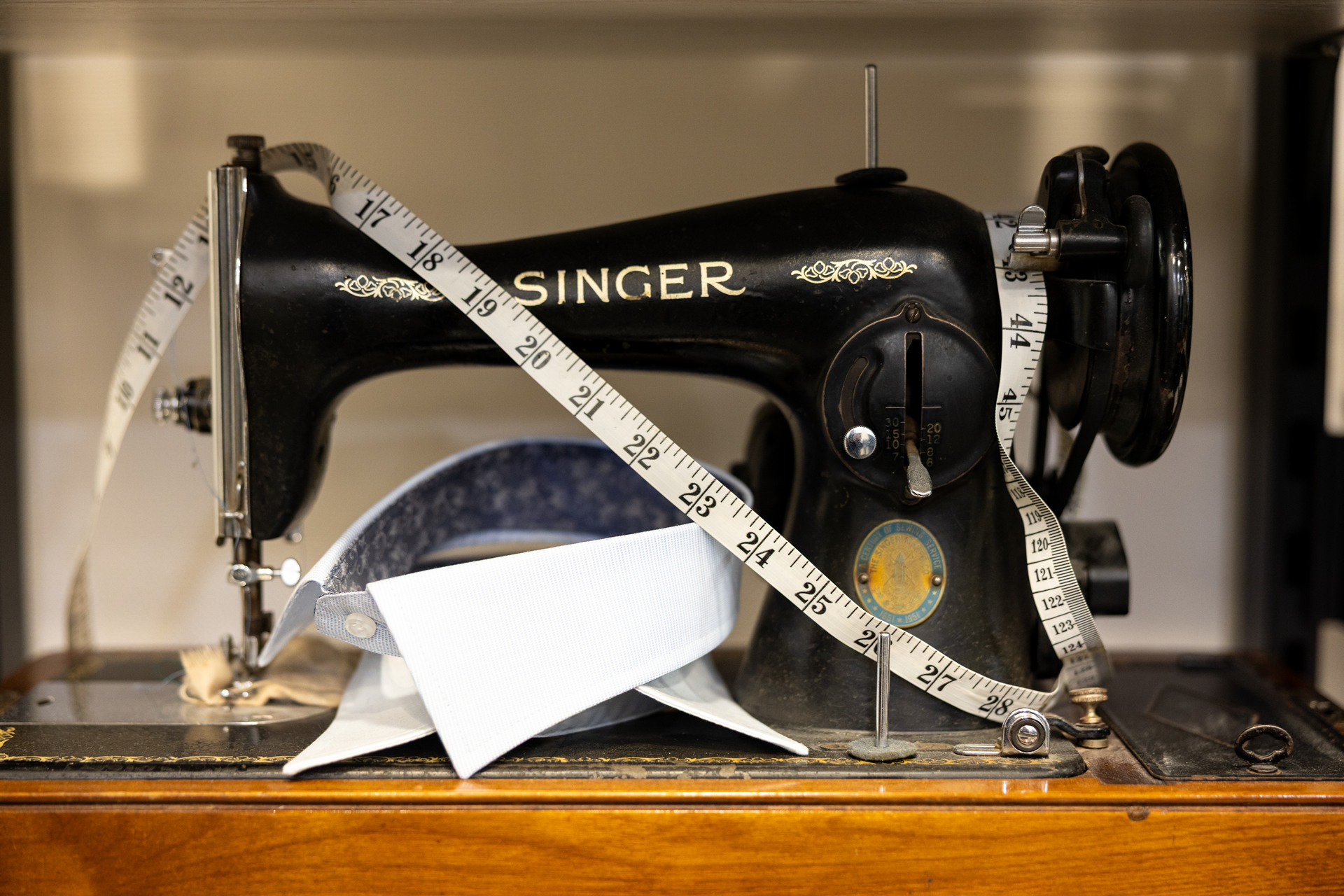 A vintage Singer sewing machine with a tape measure draped across it and a shirt collar being fitted