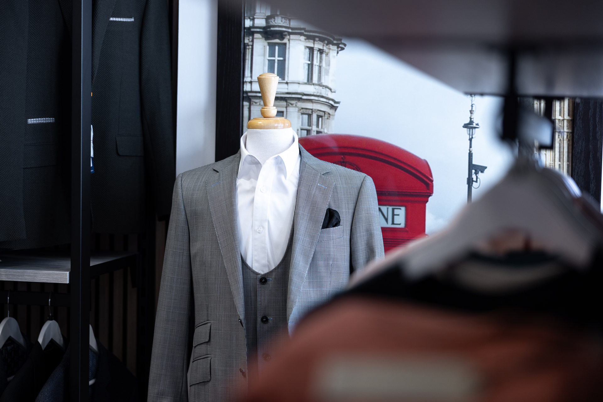 A grey plaid three-piece suit on a mannequin bust, styled against a London telephone box backdrop