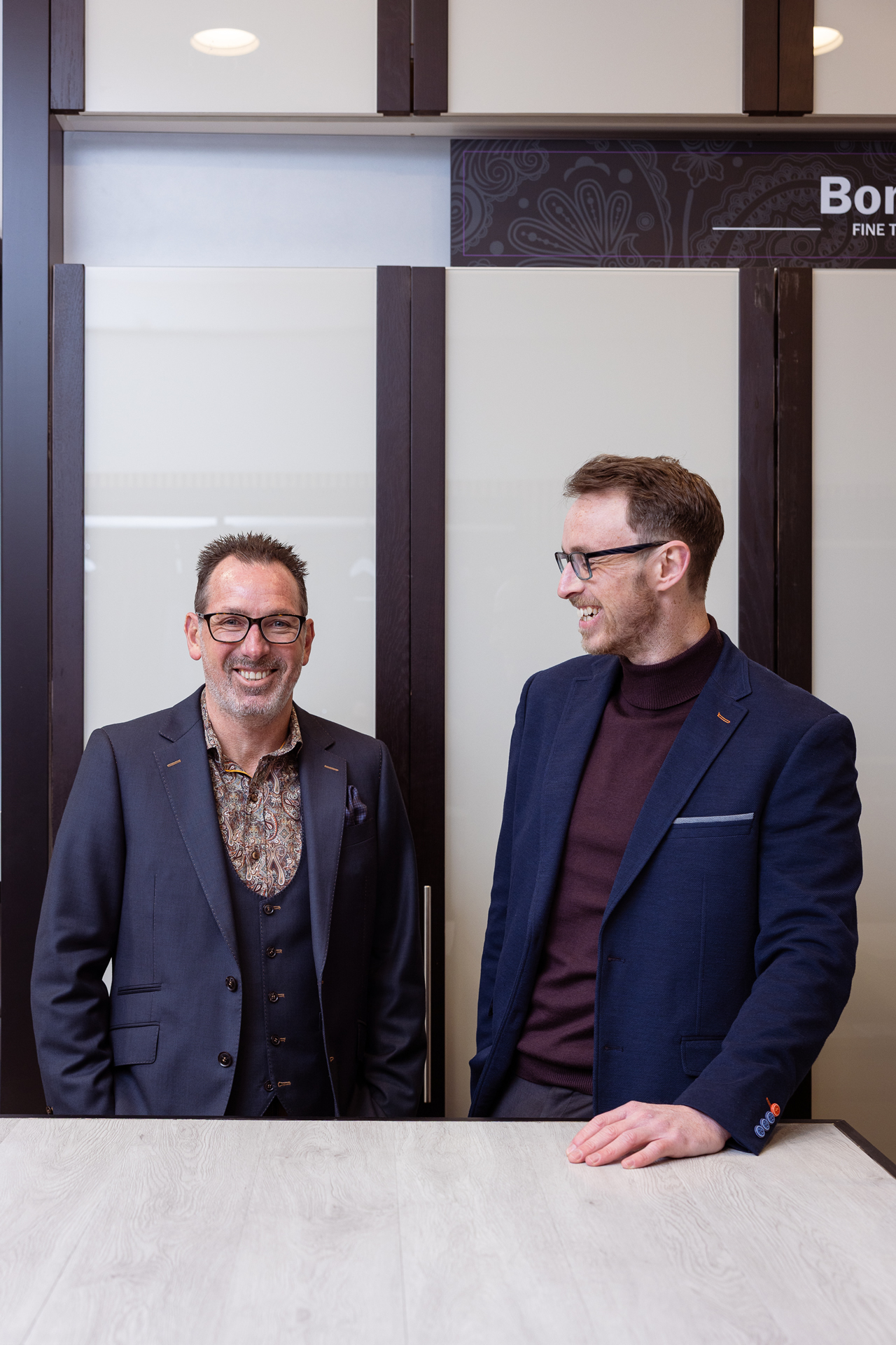 Two Bond & Co tailors in navy suits consulting together at the fitting counter